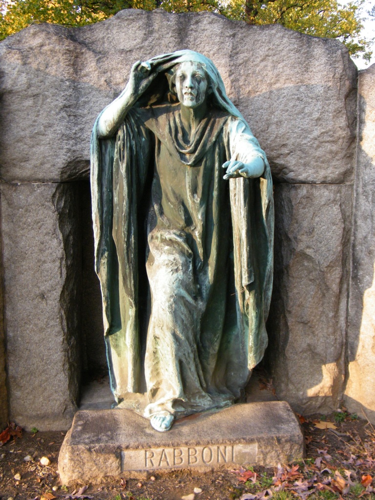 Old statue of a robed Mary Magdalene reaching out in recognition as she pulls her cloak from around her eyes. Perhaps she is crying.