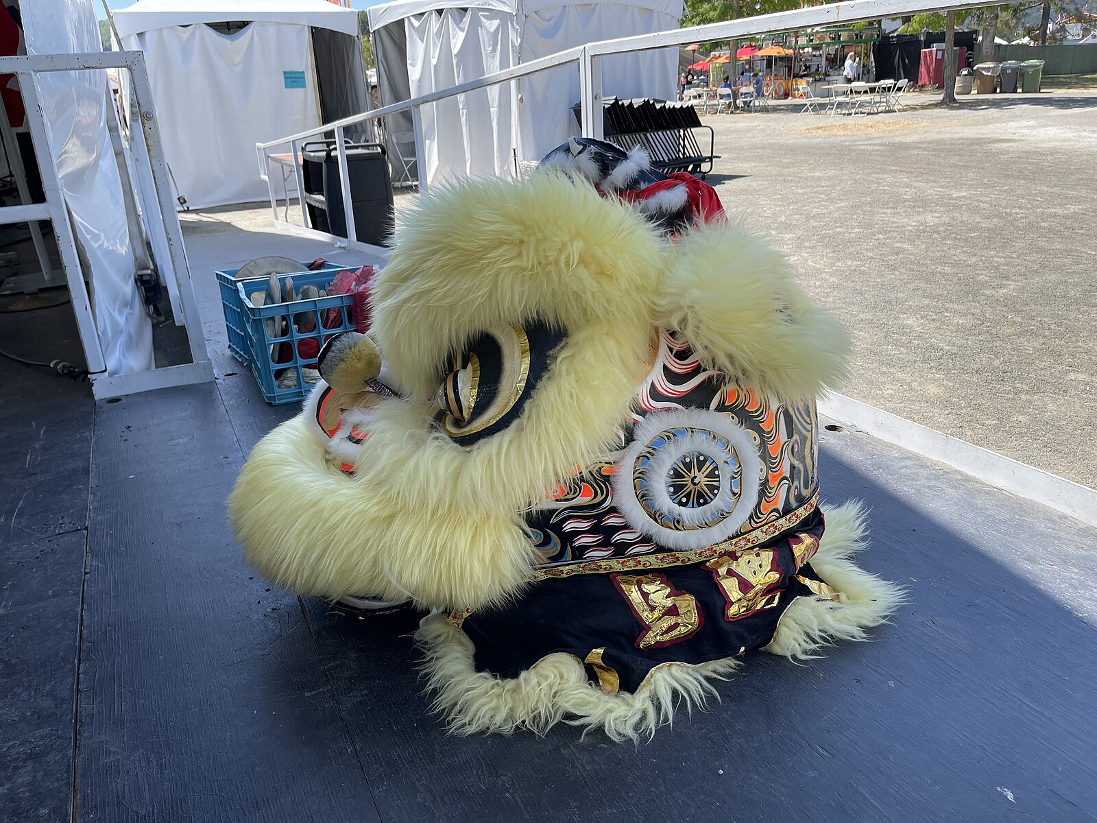 Just the head of a traditional Chinese lion dance costume, extremely fluffy and yellow, bedazzled with shiny fabrics and with large curious eyes.