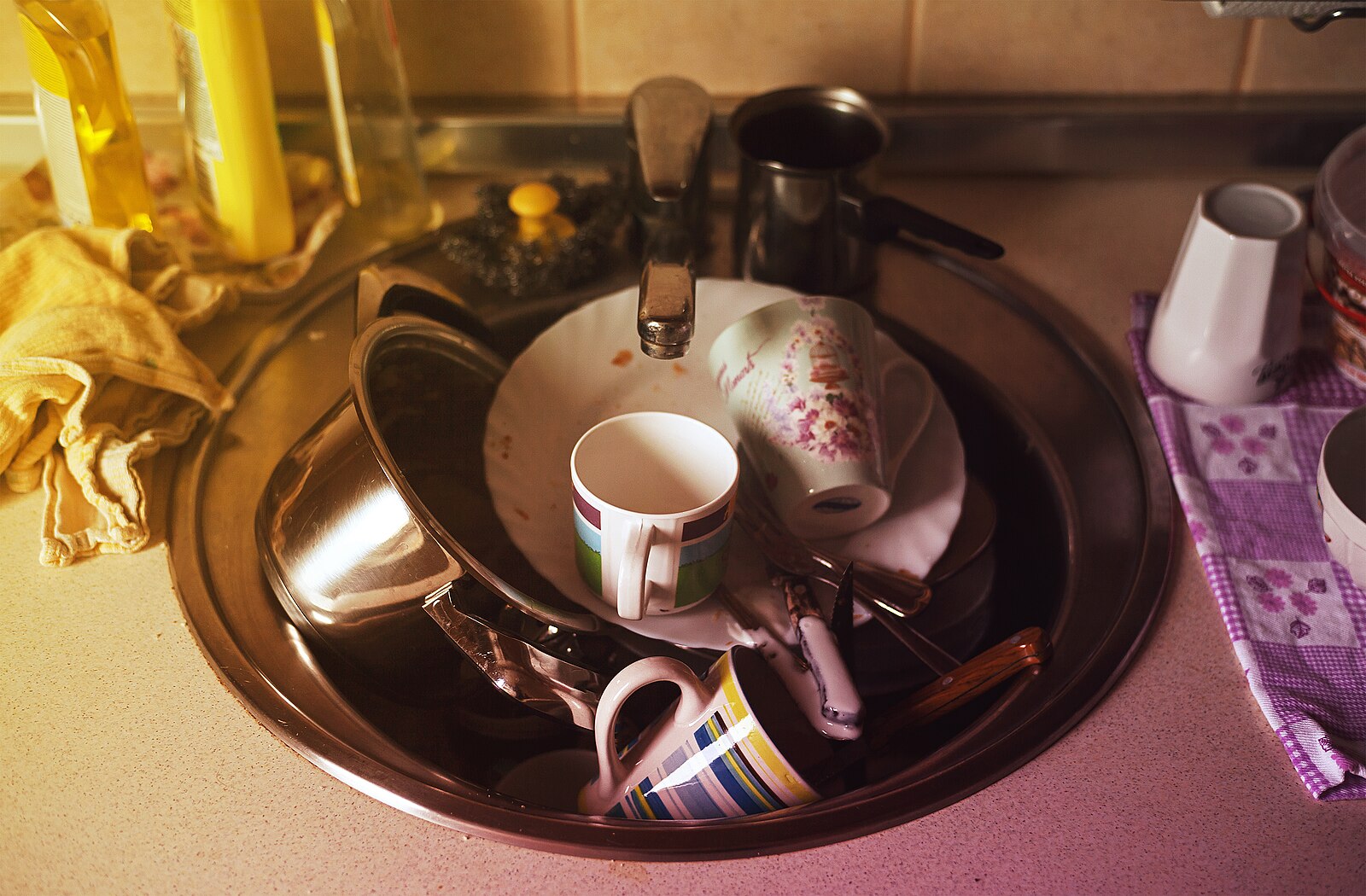 A kitchen sink full of dirty dishes: mugs, plates, cookware and cutlery